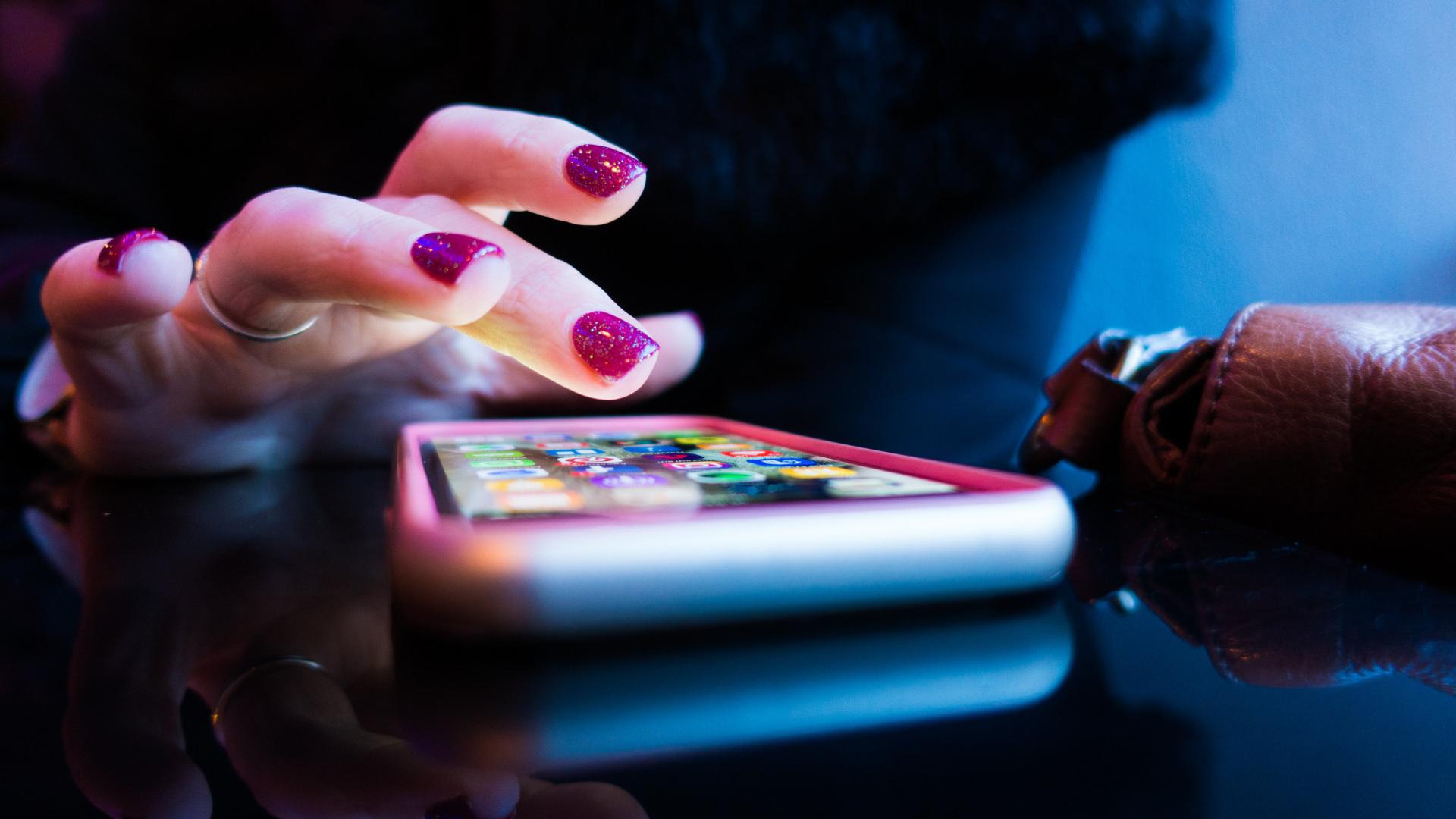 Fotografia das mãos de uma mulher tocando na tela de um smartphone