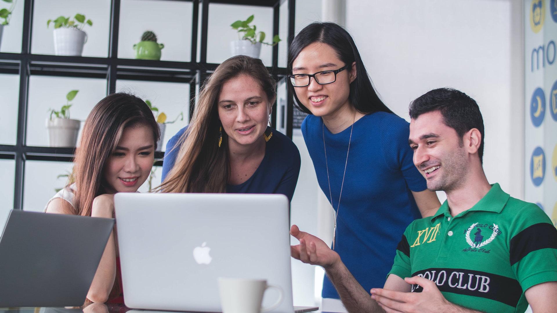 Fotografia de uma equipe de três mulheres e um homem em frente a um laptop